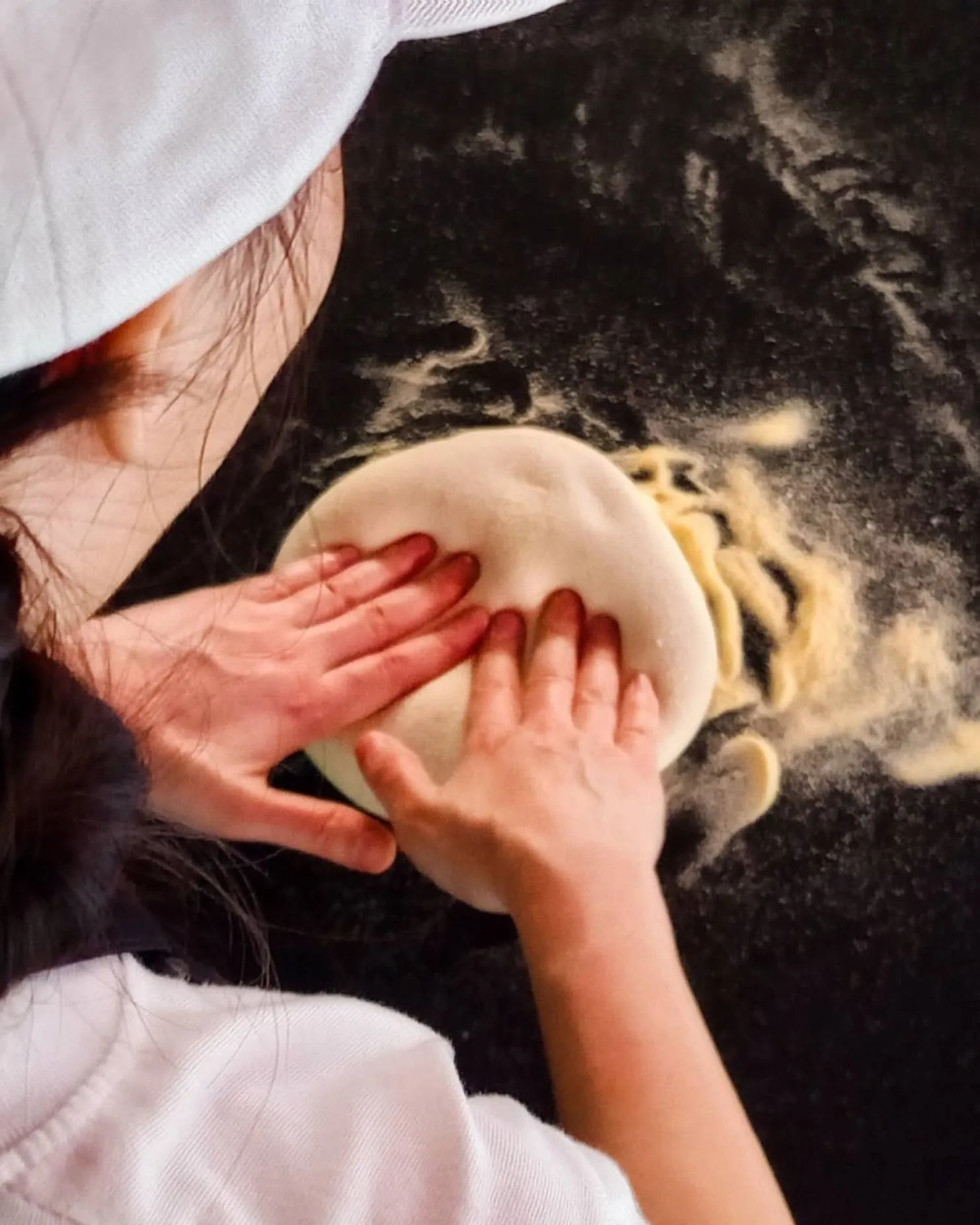 A pizzaiolo pressing a disc of dough flat with both palms on the semolina-dusted bench